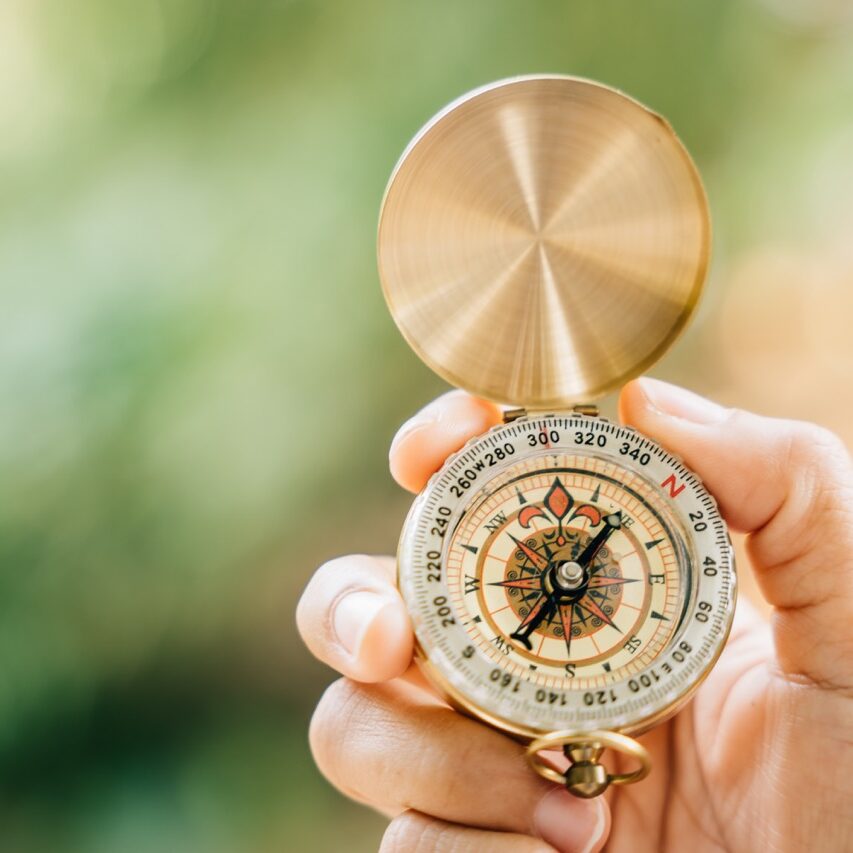 A close-up of a hand clutching a compass in the heart of a green forest. This image leaves space for text and signifies travel lifestyle and the strategic management of a thriving business.